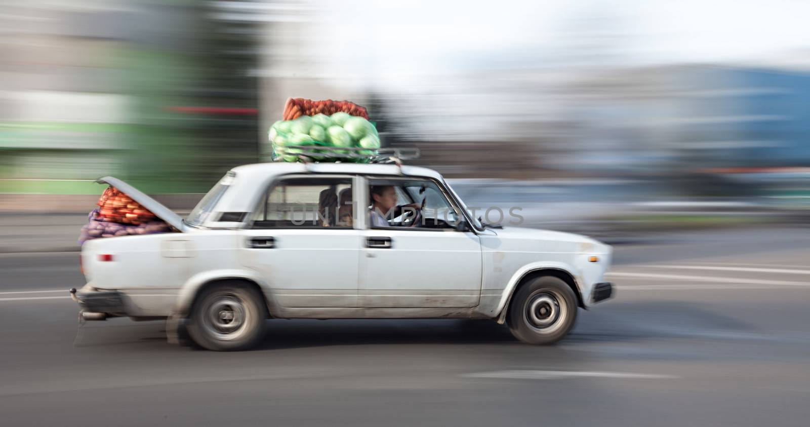 Old car loaded with cabbage and carrots rides through the city streets. Intentional motion blur