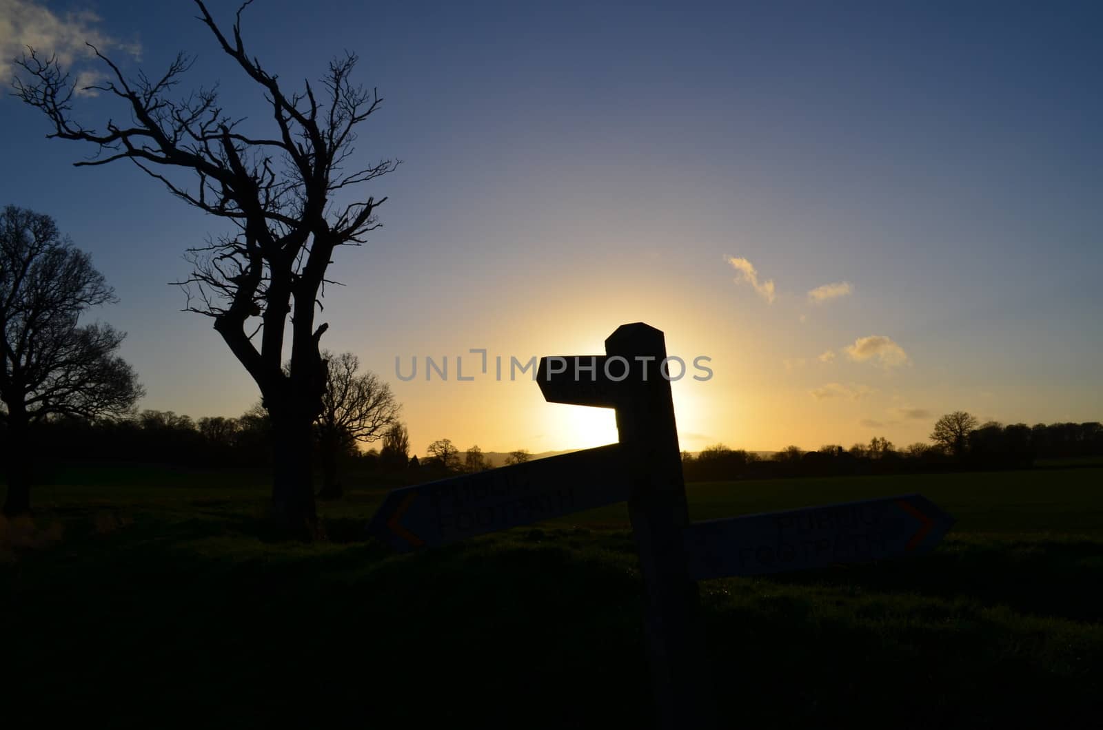 The sun sets over open countryside in England with a public footpath signpost pointing the way for ramblers.