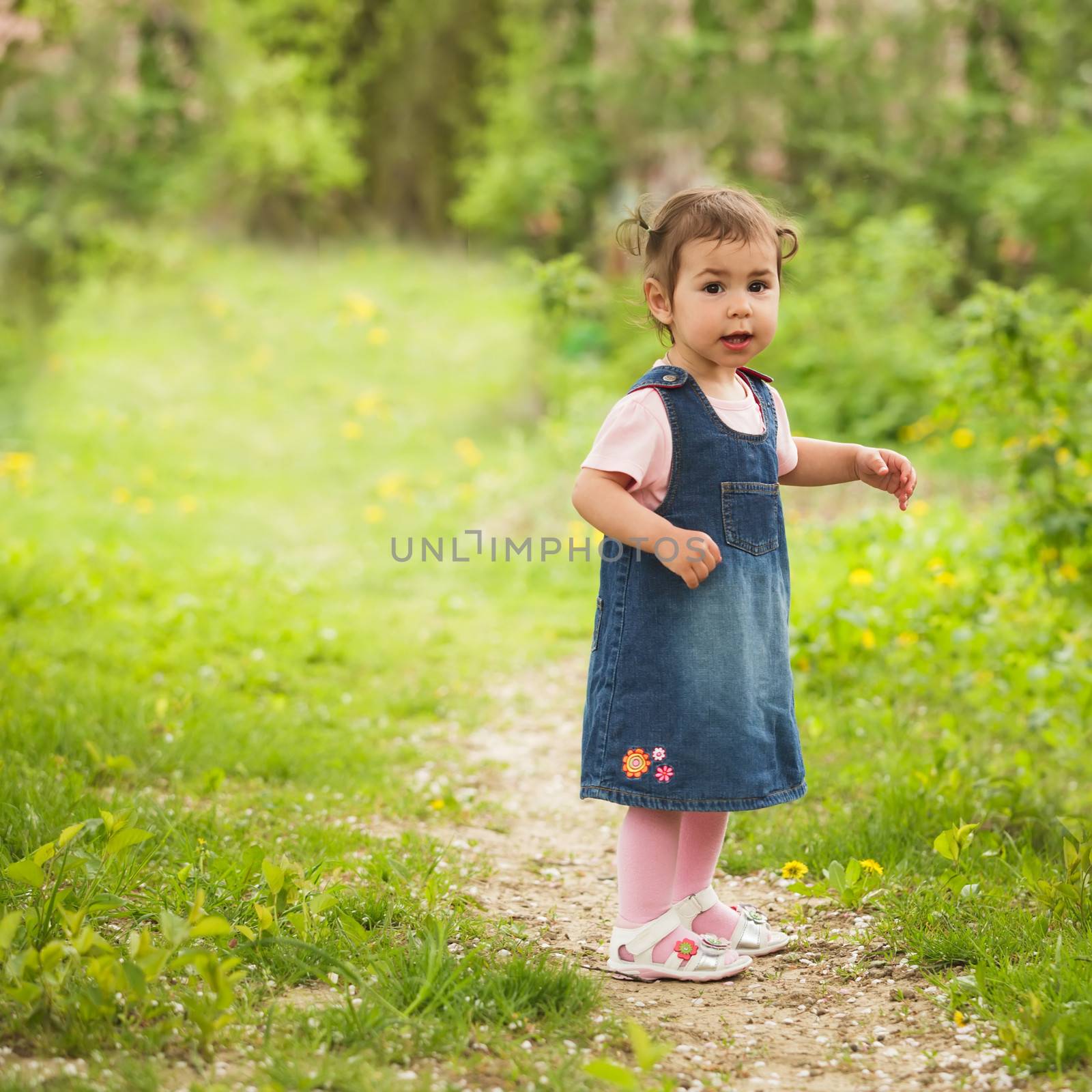 Little adorable girl in the garden, walks on the path