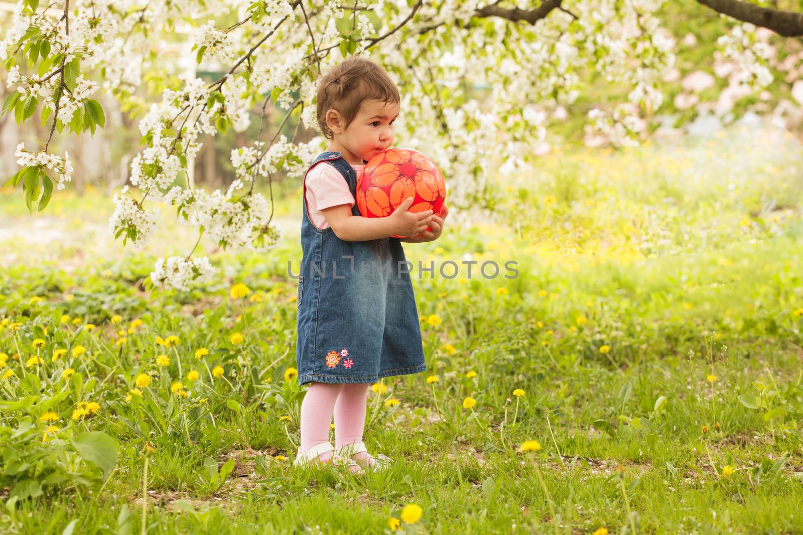 Little adorable girl in the garden, plays with ball