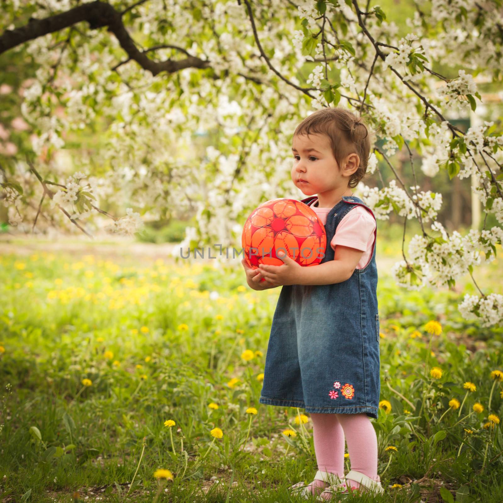 Little adorable girl in the garden, plays with ball