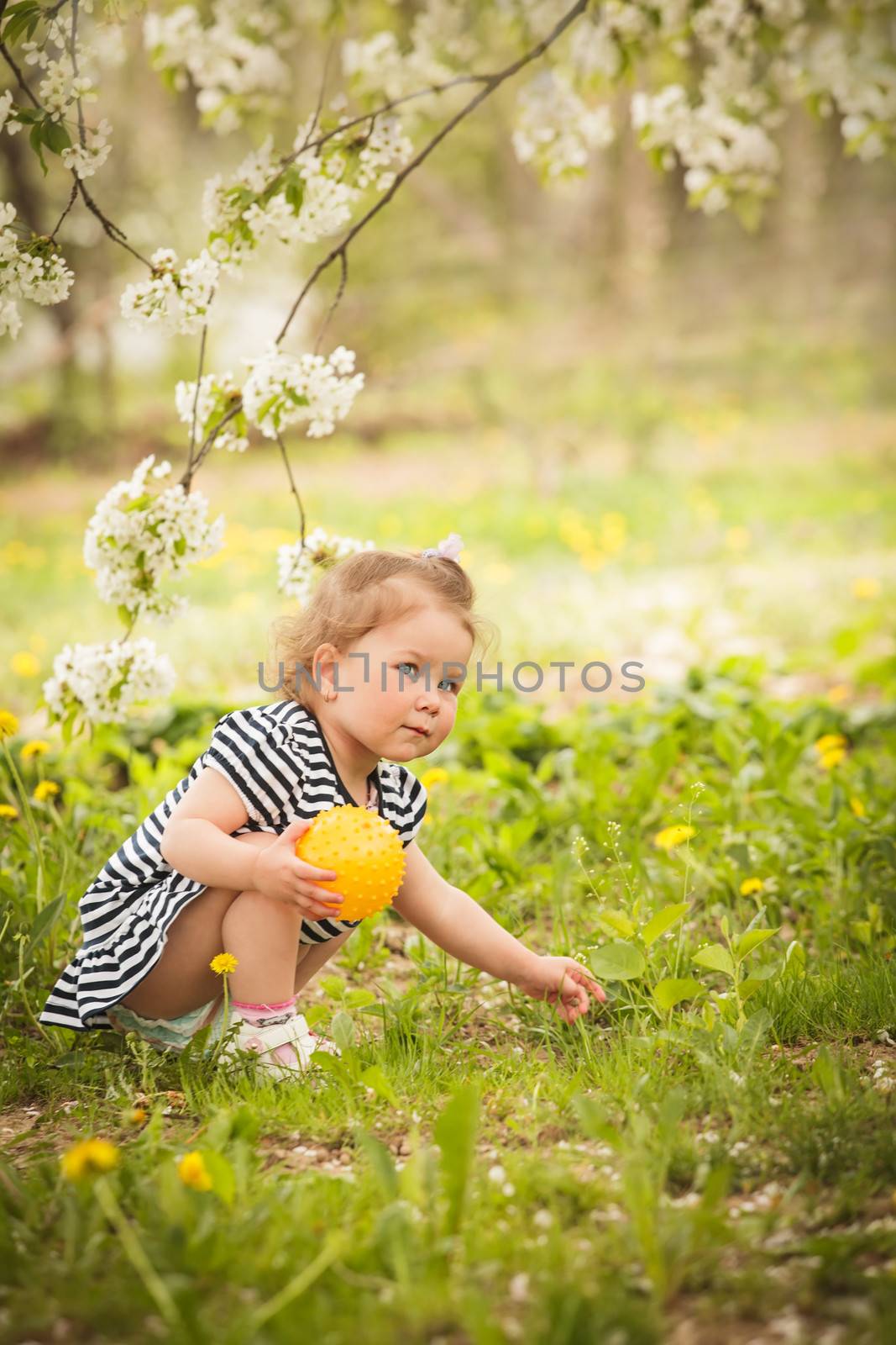 Little adorable girl in the garden, plays with ball