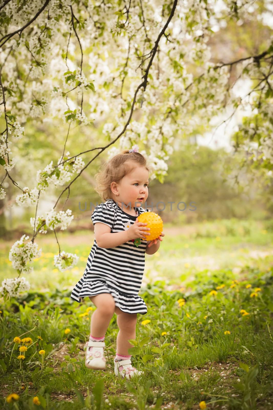 Little adorable girl in the garden, plays with ball