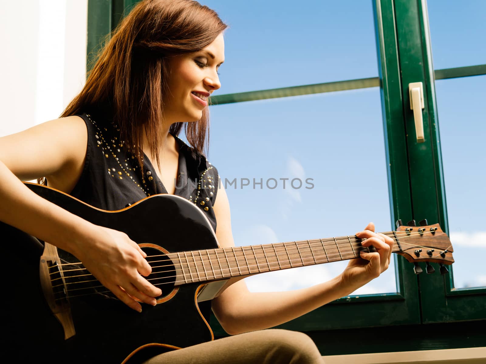 Smiling woman playing guitar by a window by sumners