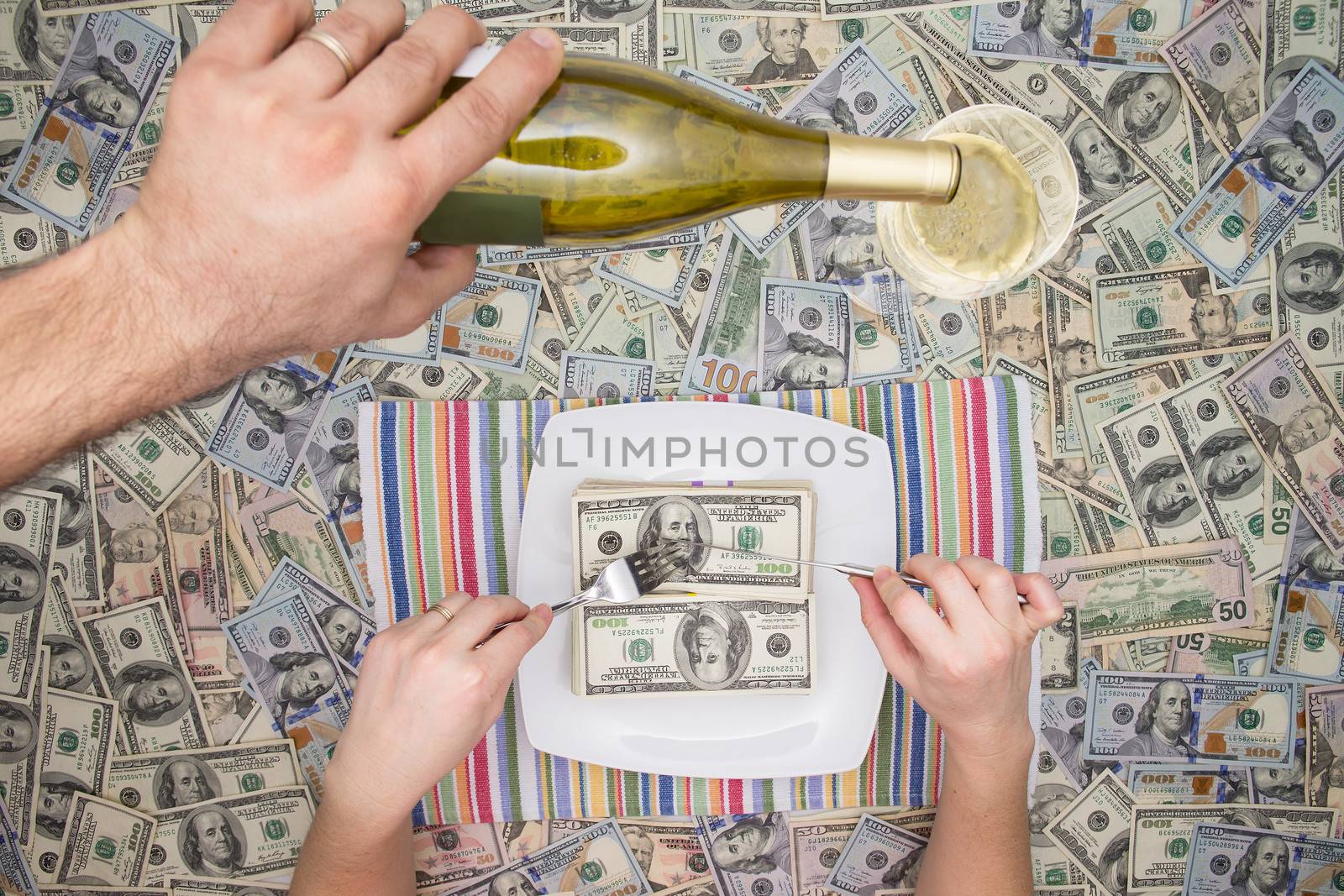 Man eating dollar bills as a servant pours champagne from a bottle overhead on a background of money in a conceptual image of wealth and extravagance