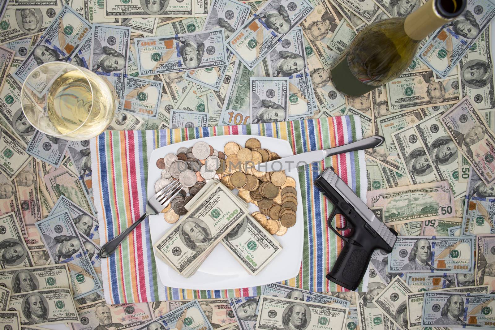 Overhead view of a place setting with a plate of money, a handgun and champagne on 100 dollar bills depicting wealth through crime and racketeering or celebrating a win and keeping it secure