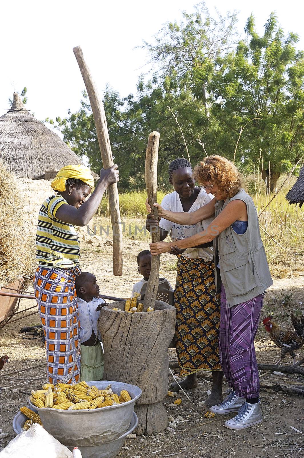 a French tourist participates in folding corn in good spirits with women from a village in Burkina Faso