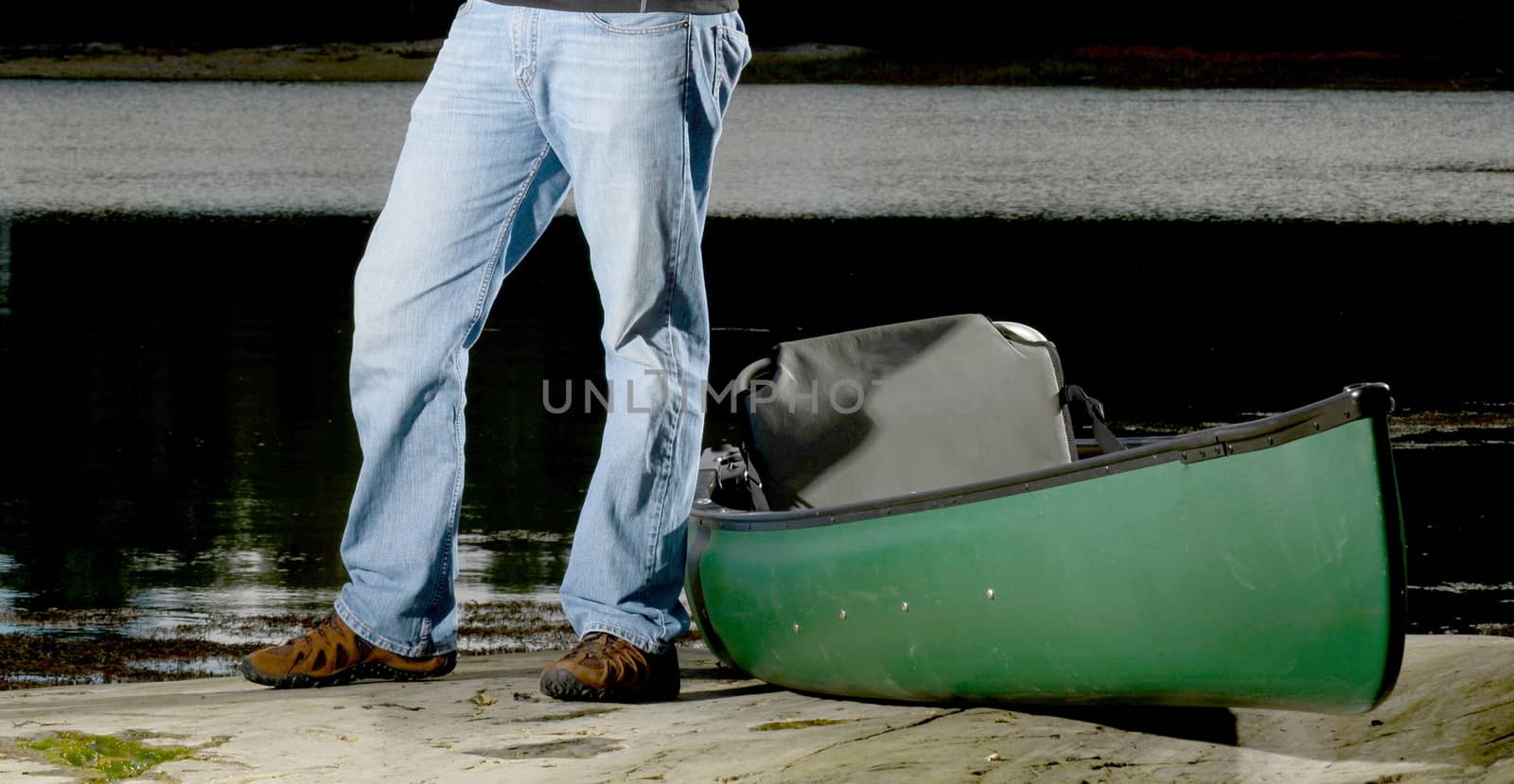 man standing with a green canoe on the edge of a river