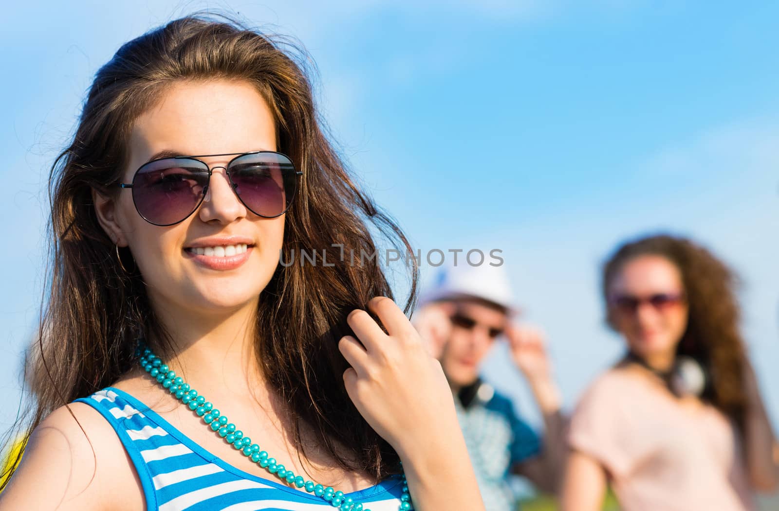 stylish young woman in sunglasses on the background of blue sky and friends