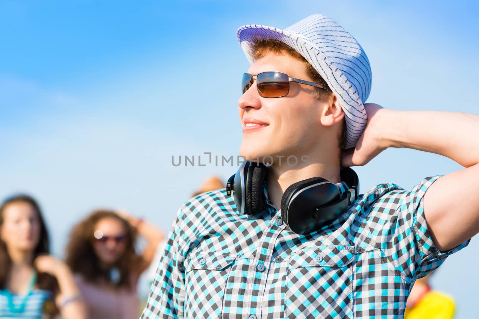 young man in sunglasses, a hat holds a hand on a background of blue sky and friends