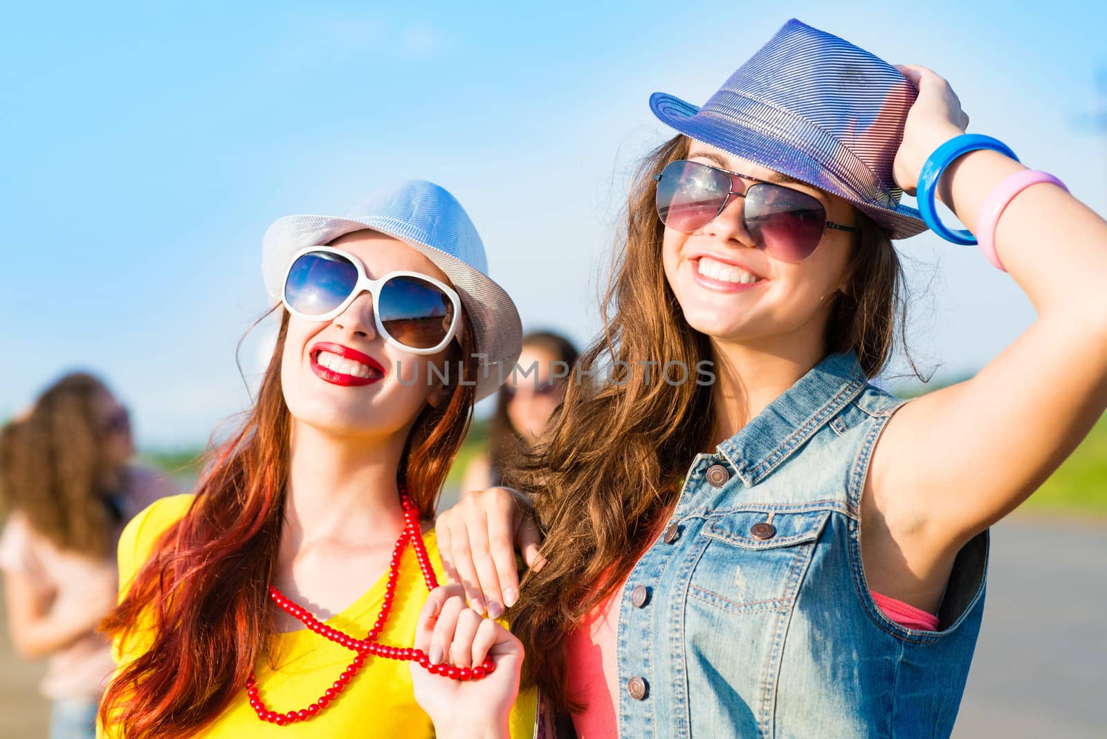 Two young girlfriends having fun on the background of blue sky and friends