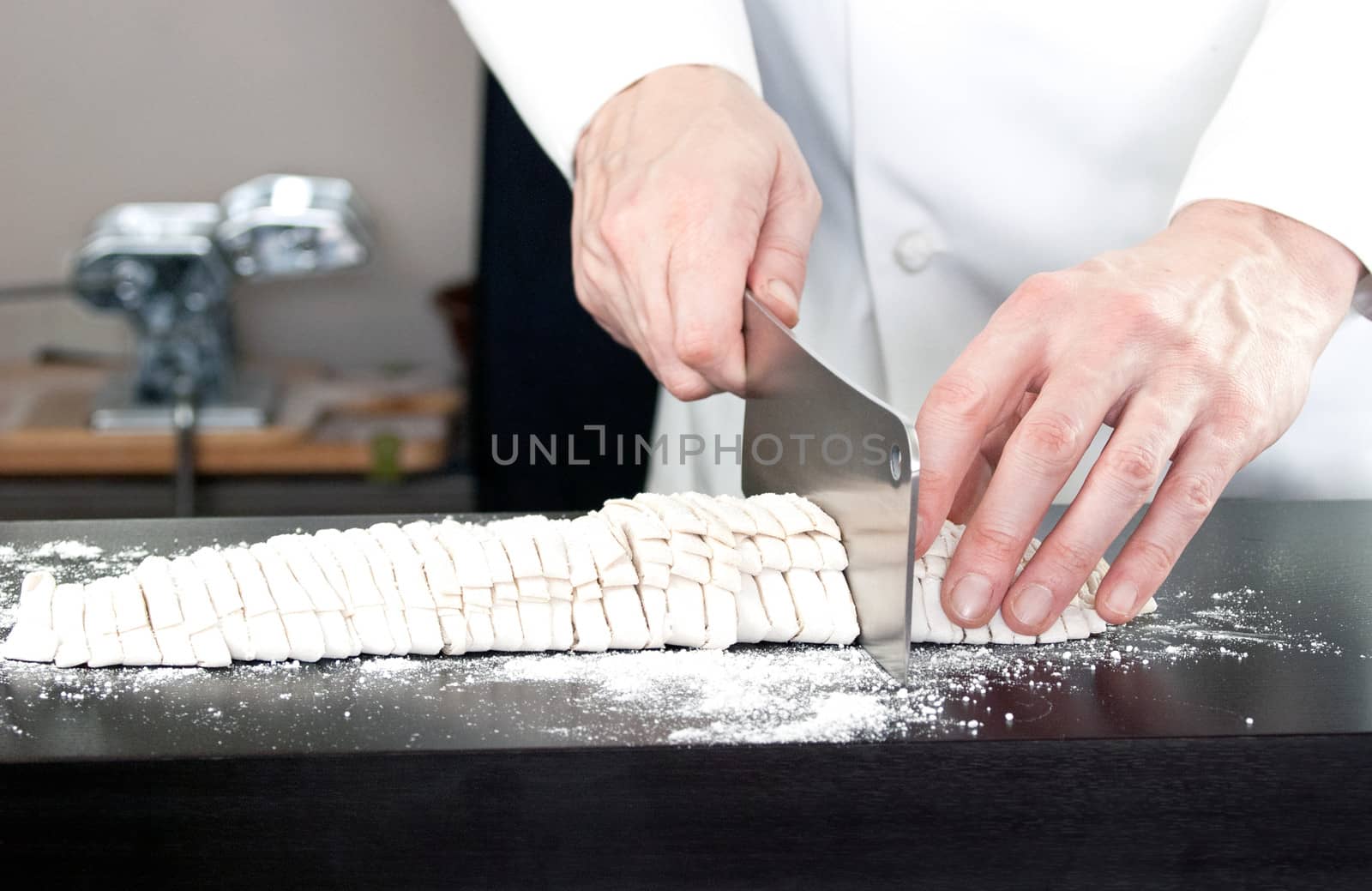 Close-up of a Chef cutting fresh noodles with a pasta rolling machine in the background.