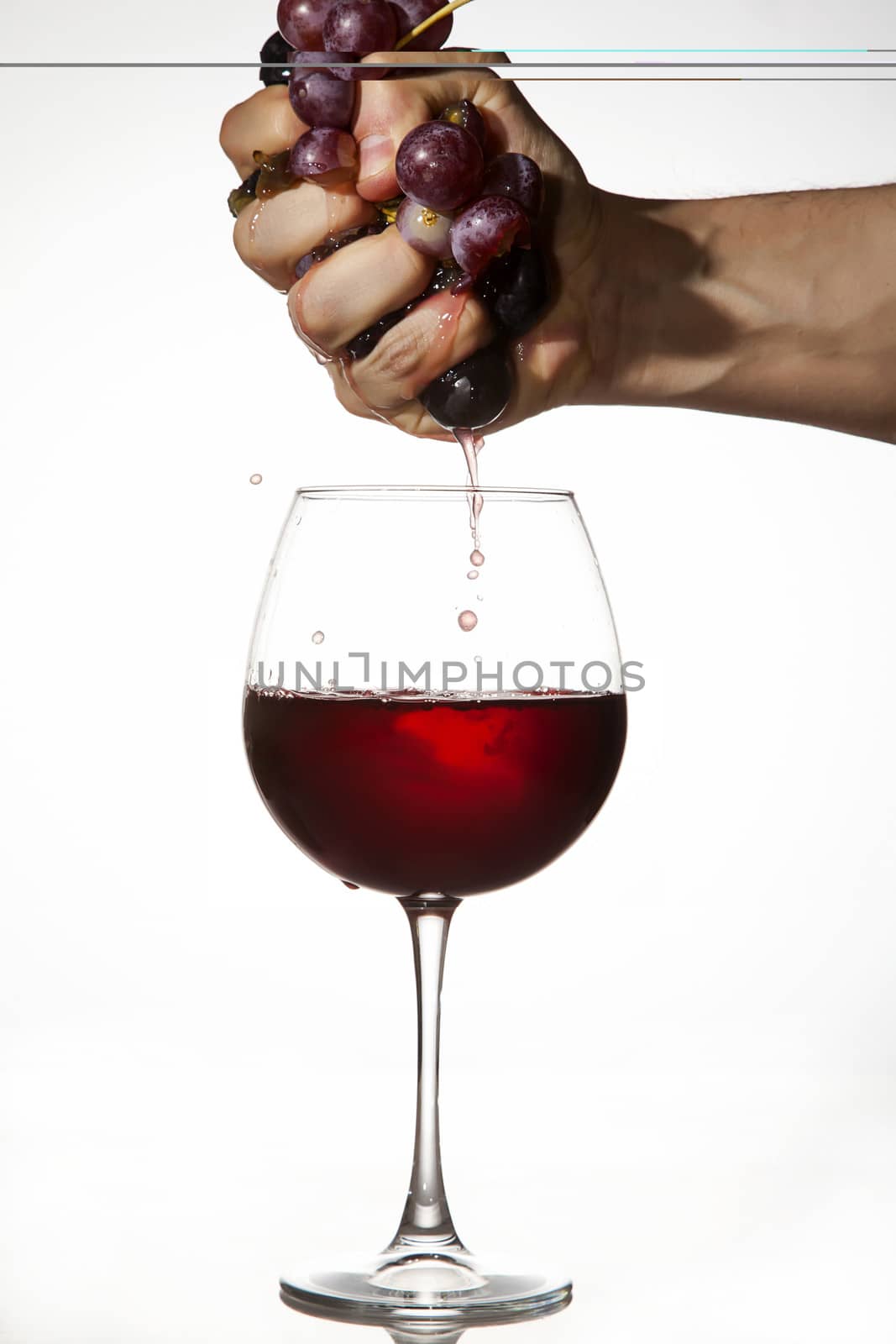 Hand is squeezing grapes to make juice over a glass of red wine