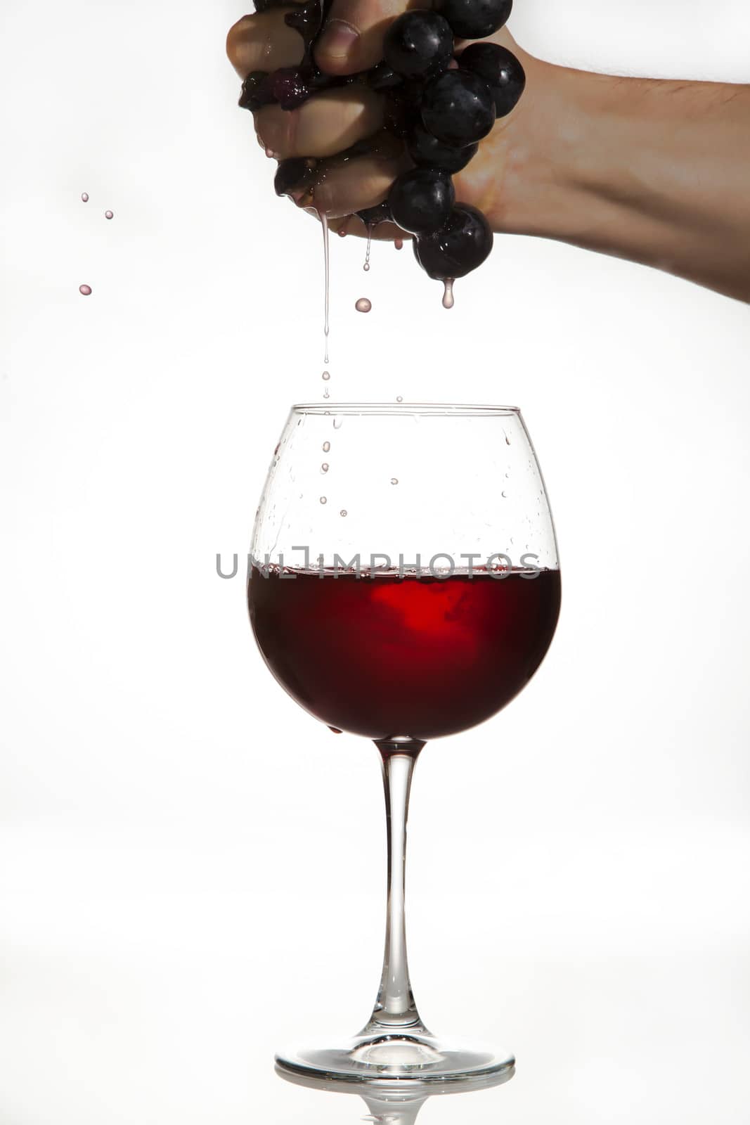Hand is squeezing grapes to make juice over a glass of red wine