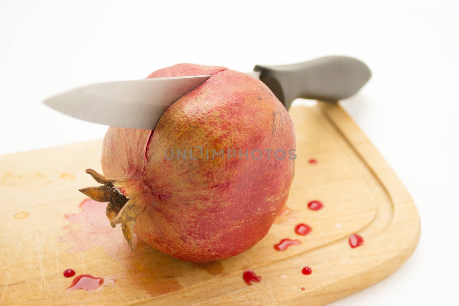 Pomegranate on a wooden cutting board with a knife inside.