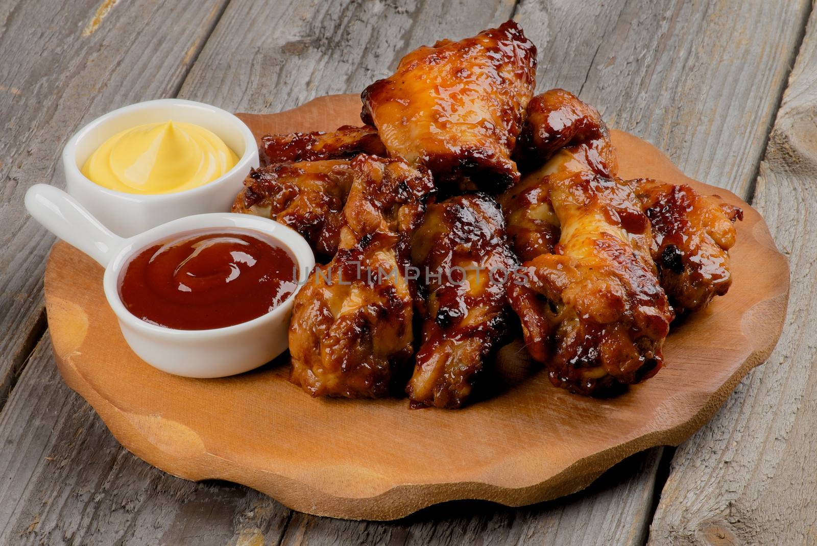 Chicken Legs and Wings Barbecue with Sauces on Wooden Plate closeup on Rustic Wooden background