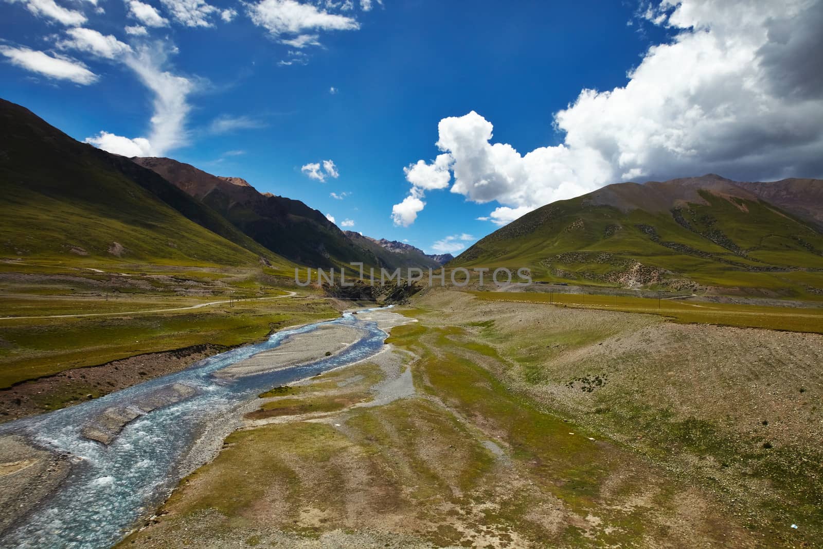 A river cross a plains in Tibetan Plateau, with mountain landscape and cloudy sky