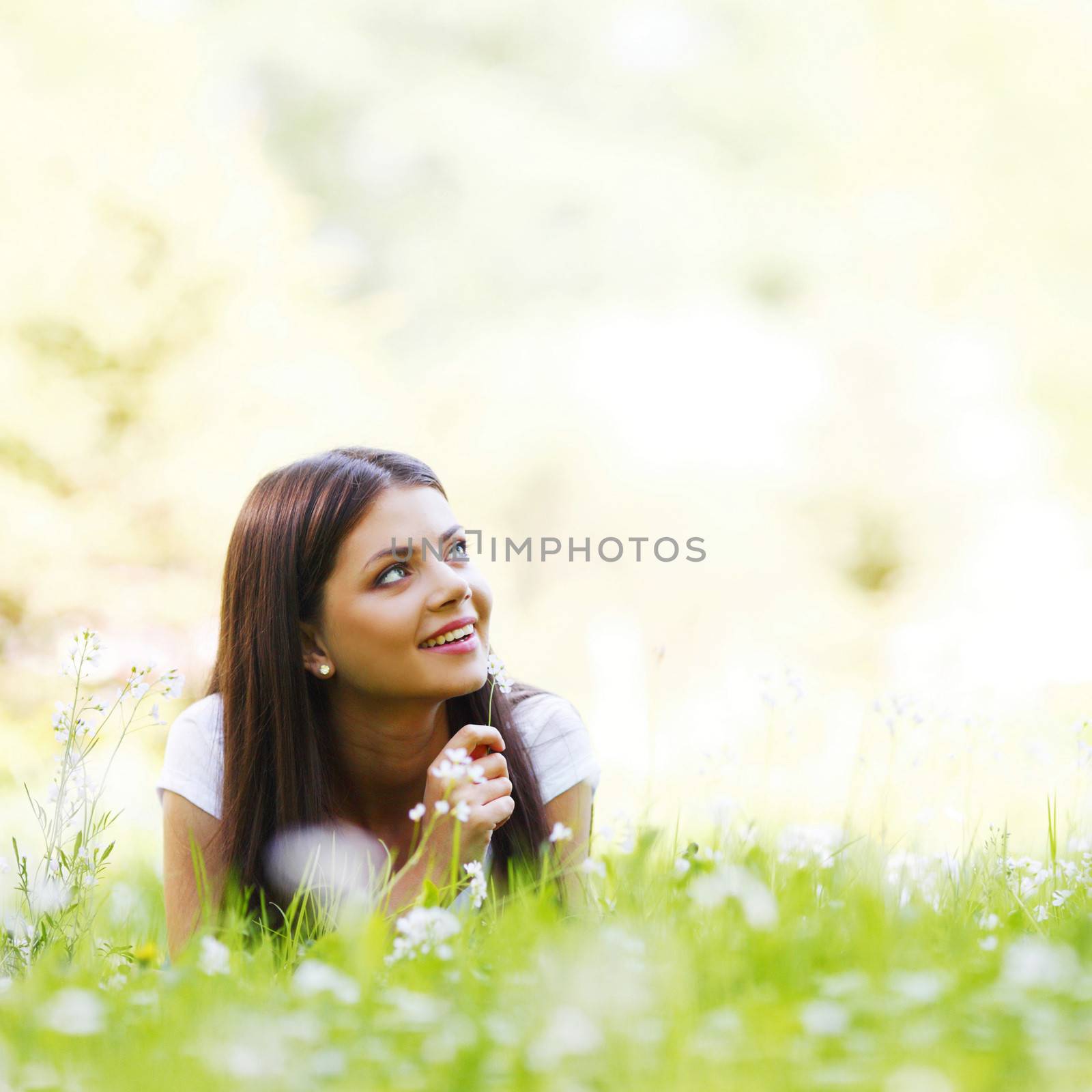 Young woman laying in sunny spring park with white flowers
