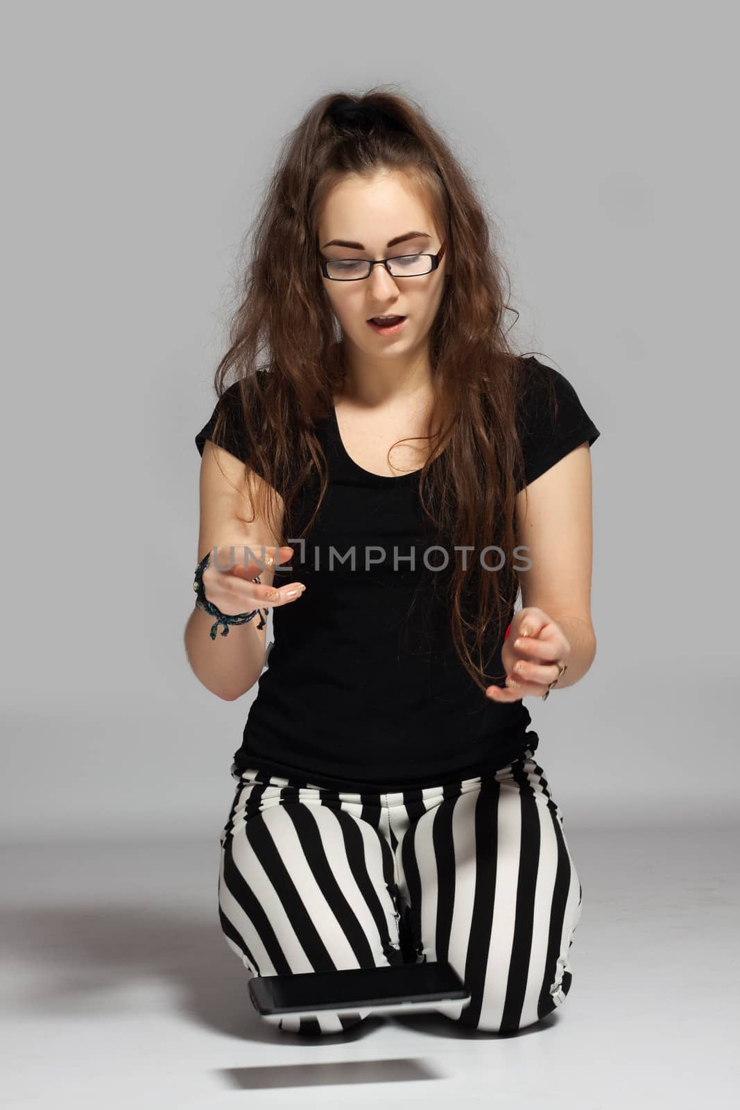 Young long-haired teenager in striped pants kneeling on the ground, dropped it out of the hand the tablet, which just falls down