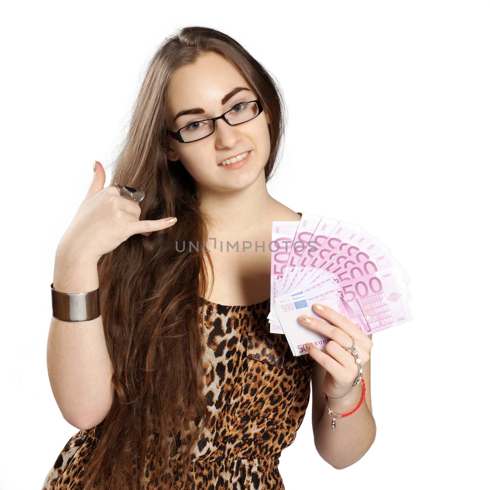 Long-haired teenager girl in leopard dress holding in hand euro as a fan and the other hand shows give me a call, isolated on white background