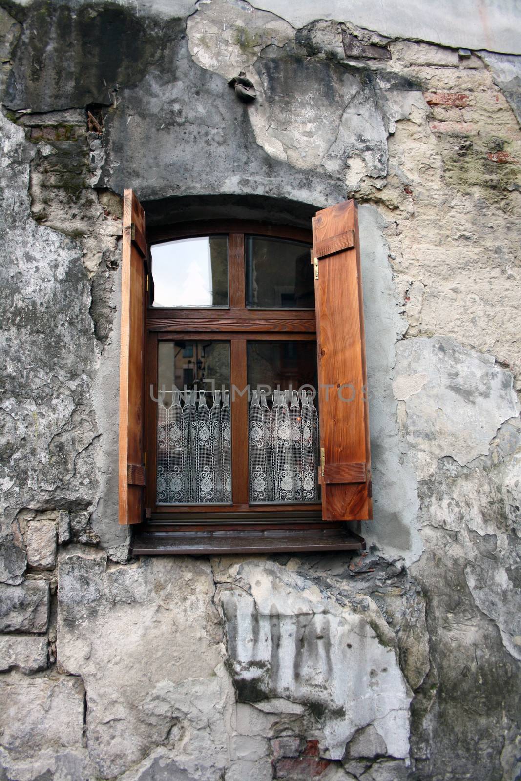 Old window with shutters and curtain on the background of a crumbling wall