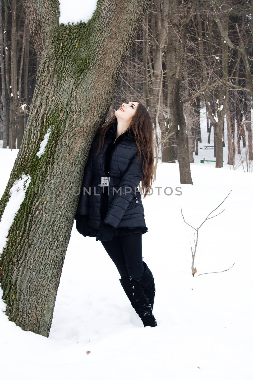 Shot of a young woman with the head near a tree in act to look 