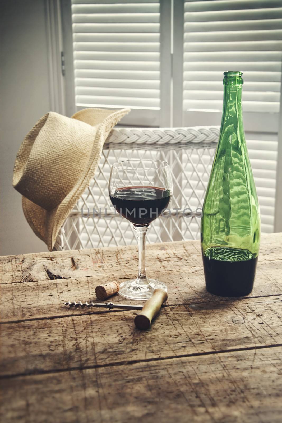 Glass of red wine standing on an old table with straw hat by Sandralise
