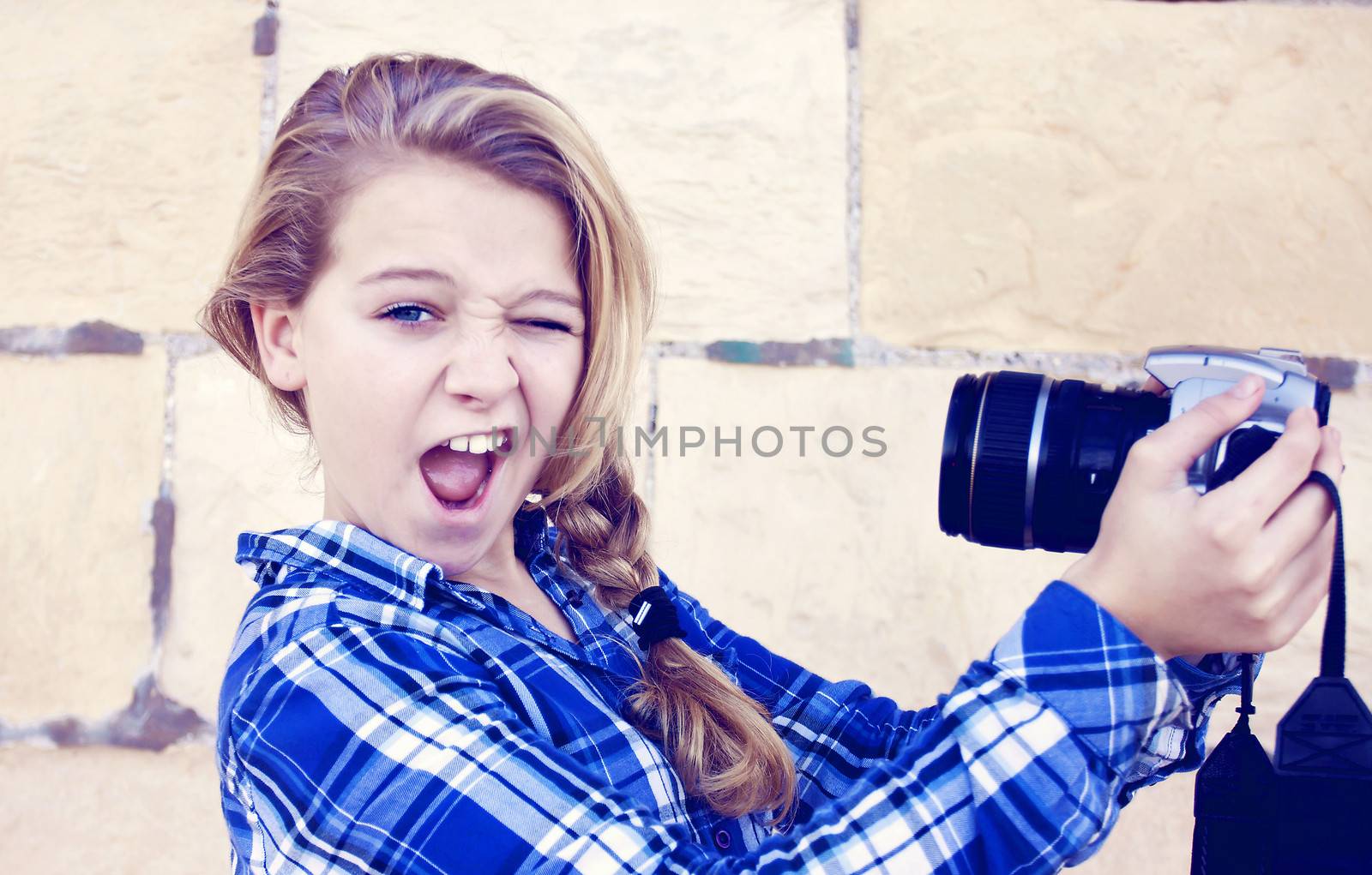 Young teenage girl doing a funny face taking a self portrait with a slr camera. Slight retro tint over image