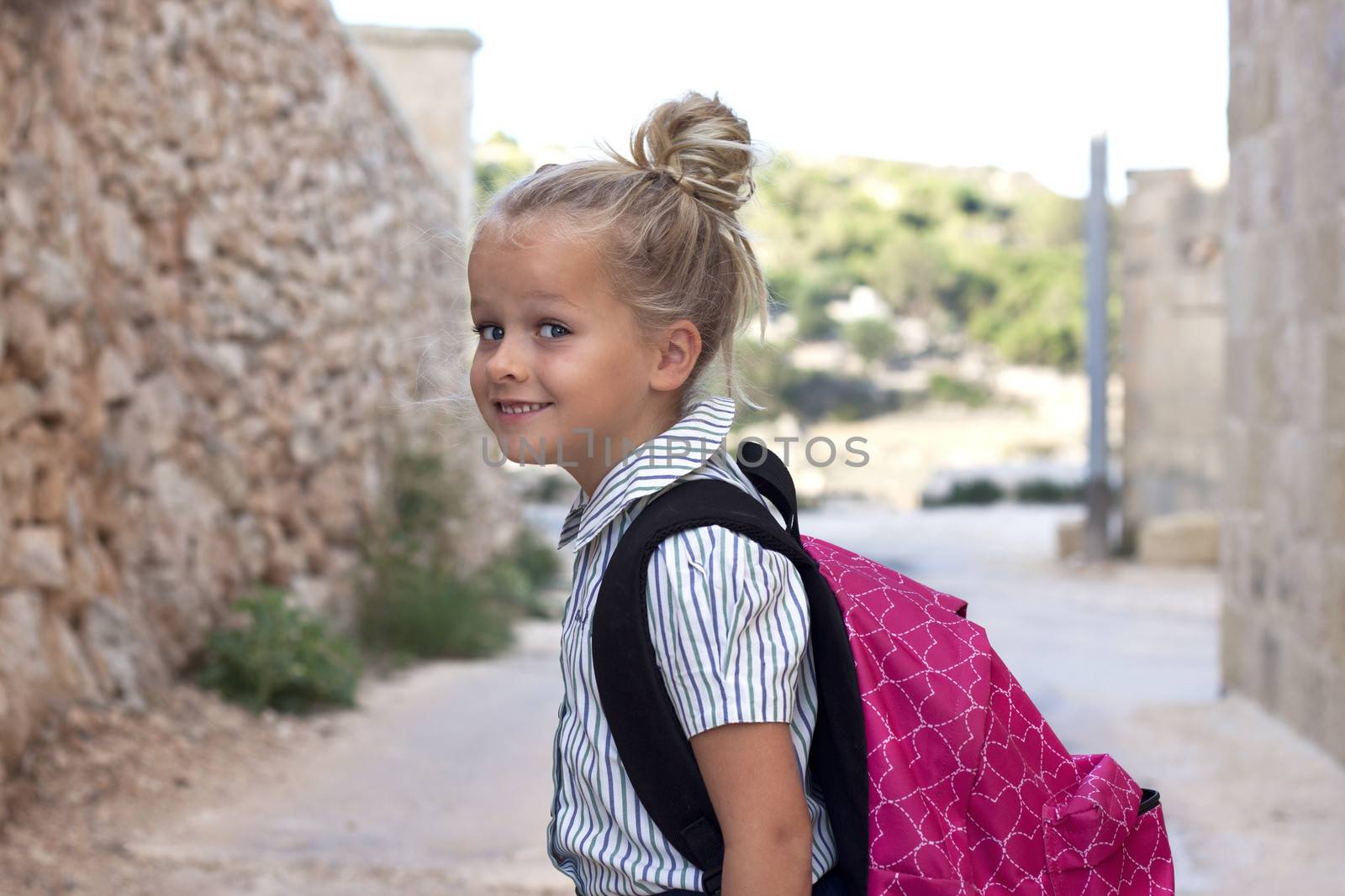 A young child with school uniform and bagpack outside, smiling, positive, looking at camera