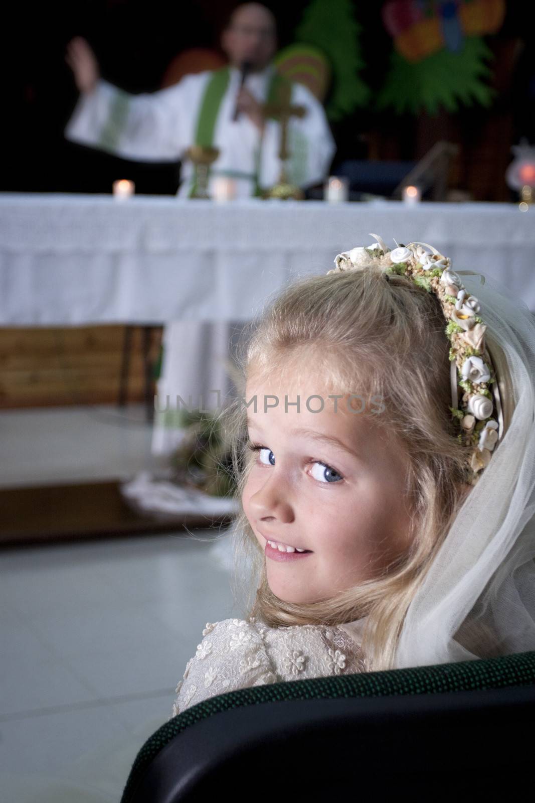 A young child doing her catholic first holy communion attending mass wtih a priest by the altar