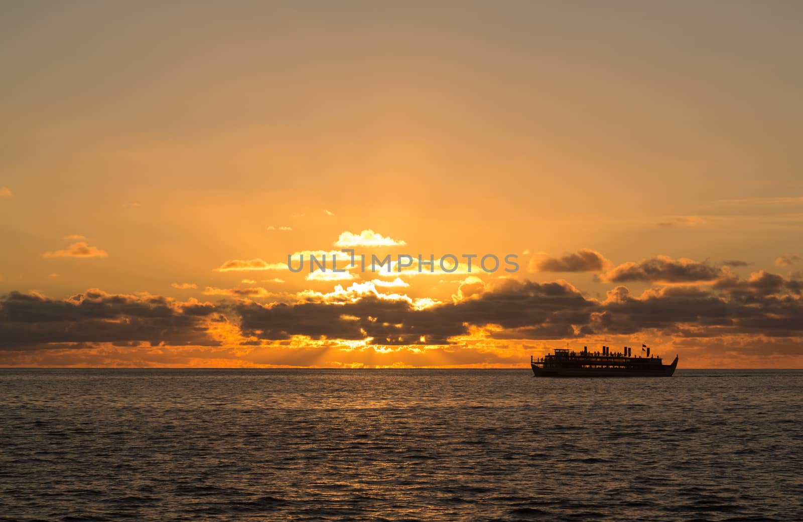 Sunset cruise ship sails on horizon as the sun sets slowly behind clouds off Oahu in Hawaii