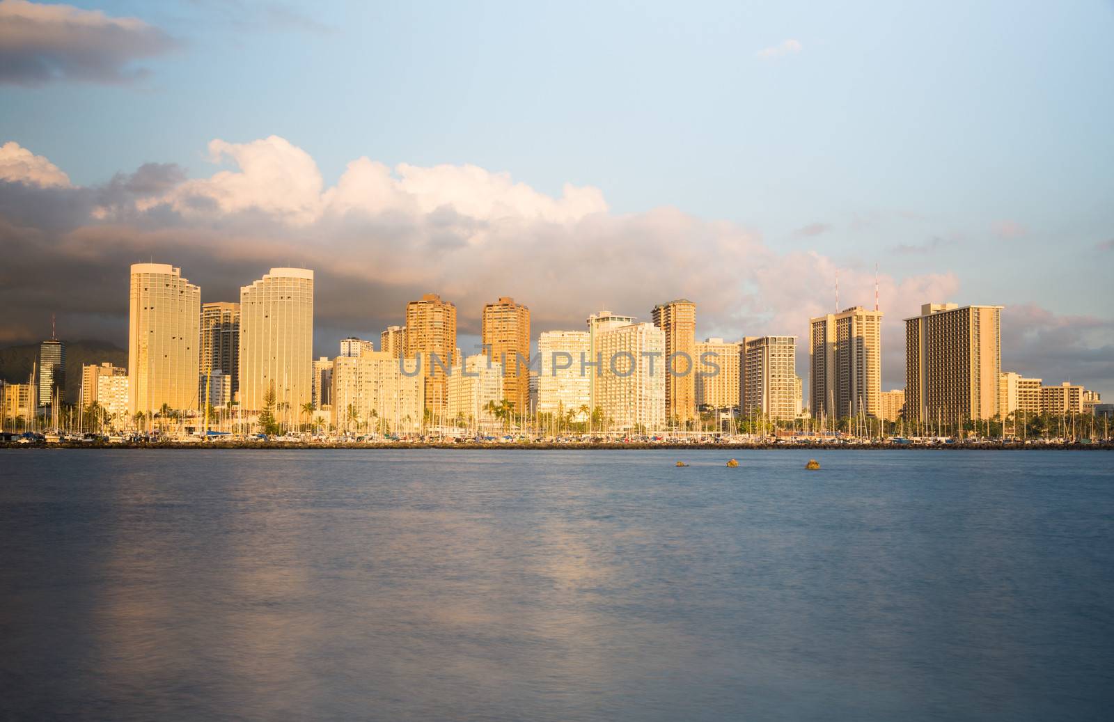Panorama of the skyline of Honolulu and Waikiki from Ala Moana park as the sun sets and illuminates the facades of the hotels and apartments