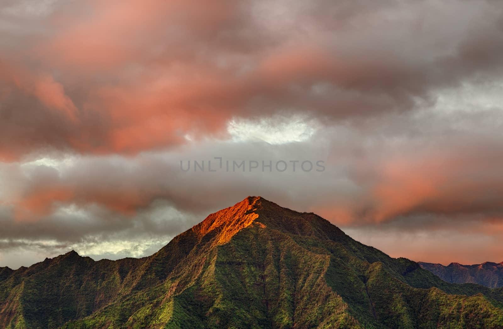 Mountains of the Na Pali mountain range in the distance above Hanalei Bay in Kauai. Taken just after dawn with the sun just skimming the peaks of the mountains and illuminating the clouds with a brilliant red light