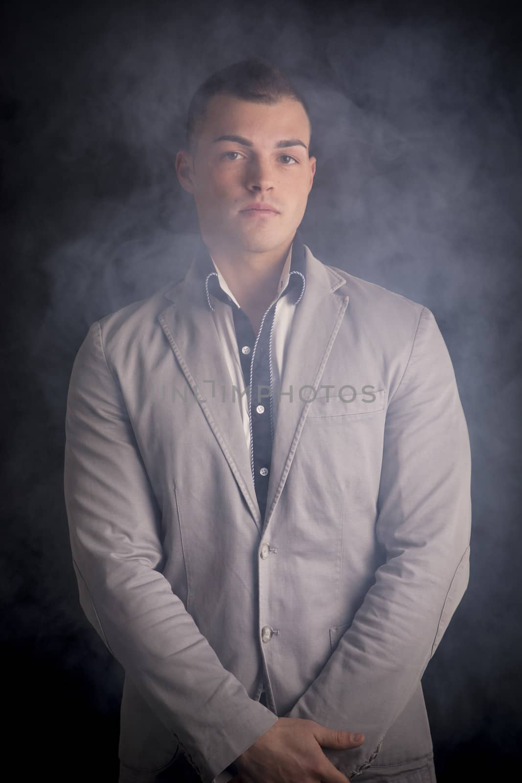 Attractive elegant young man standing with smoke around him, dark background