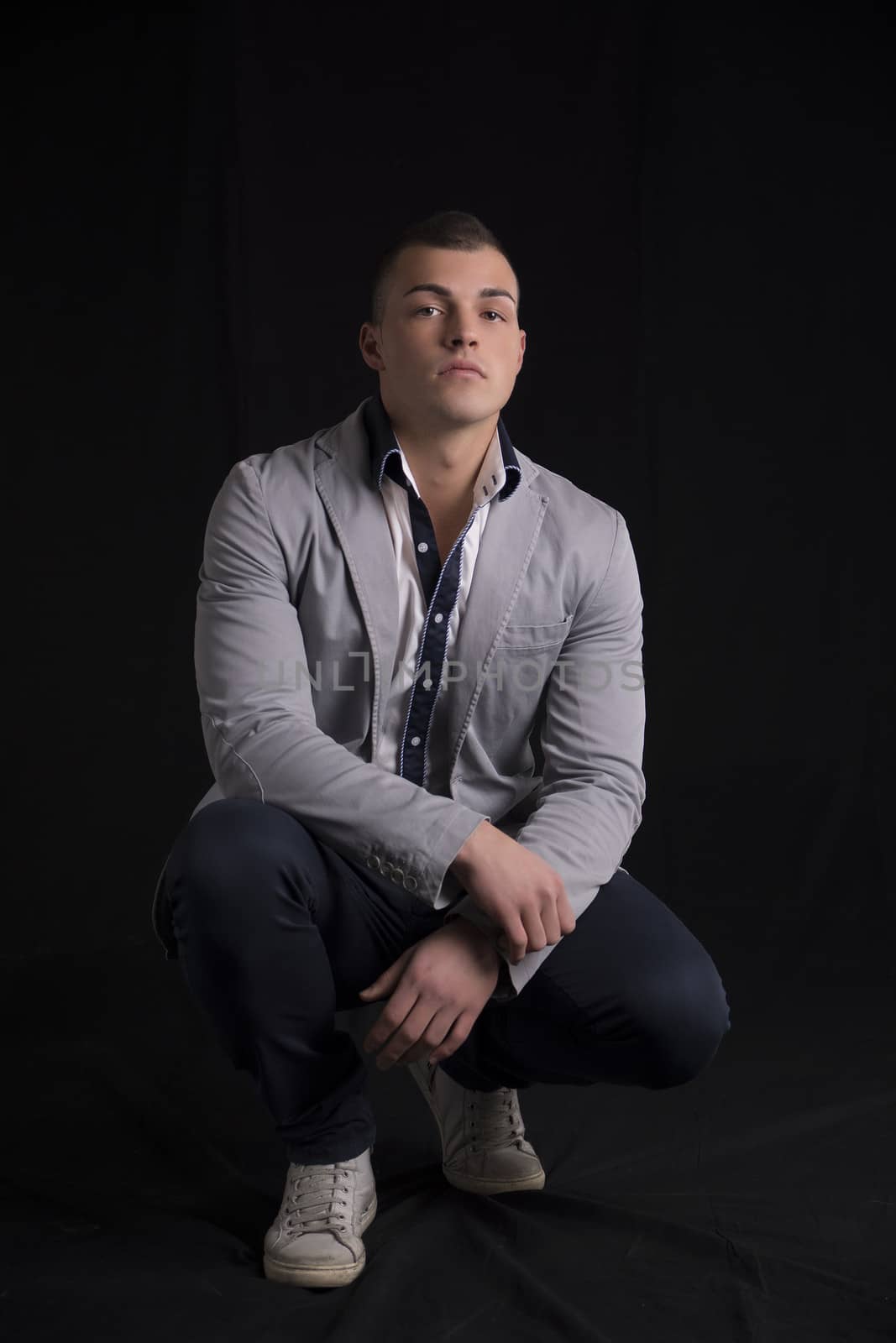 Portrait of handsome young man with shirt and jacket sitting on his heels, looking at camera