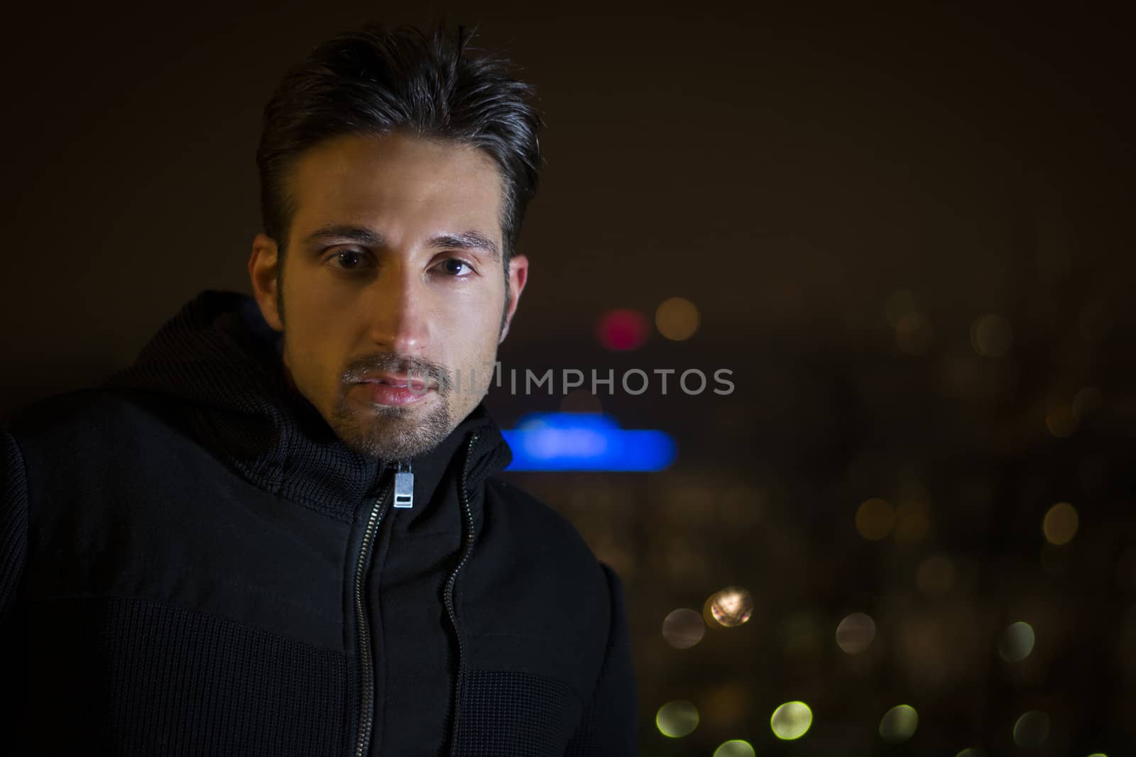 Attractive young man portrait at night with city lights behind him, looking at camera