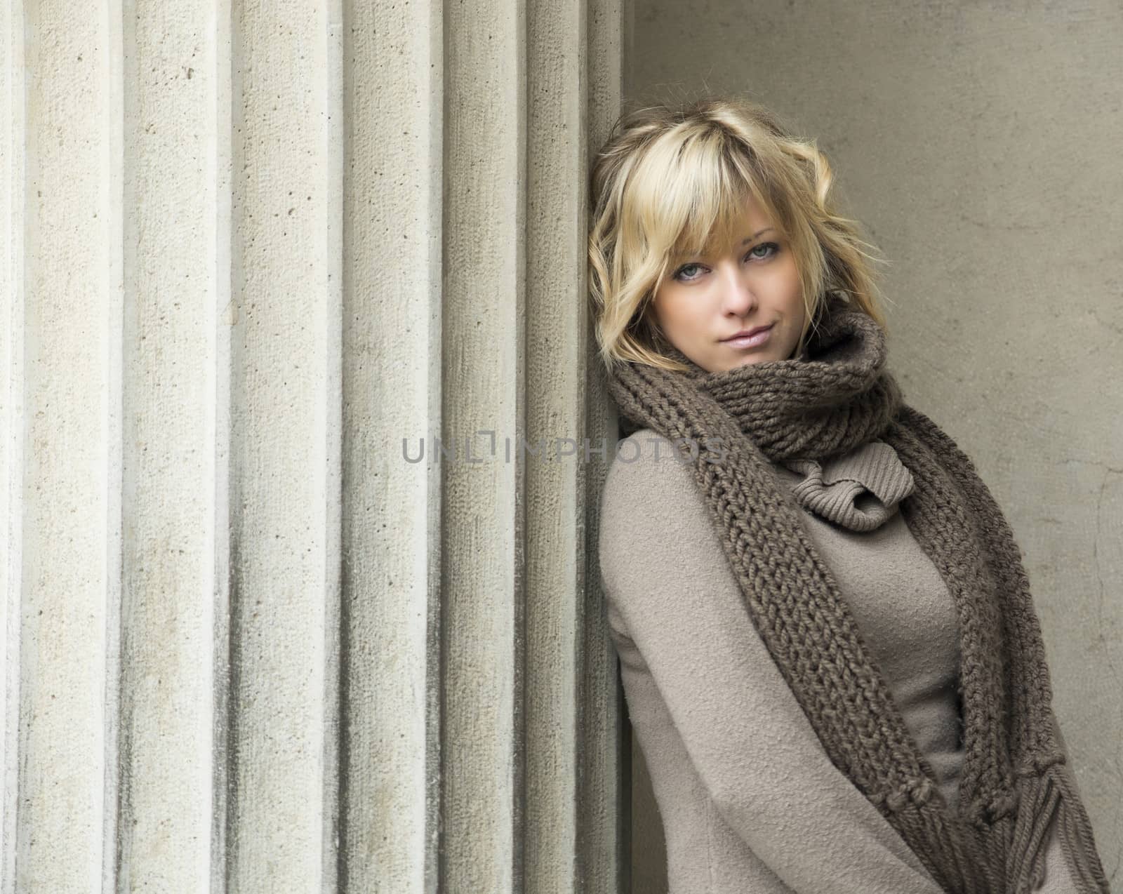 Attractive blonde young woman leaning against concrete column, looking at camera