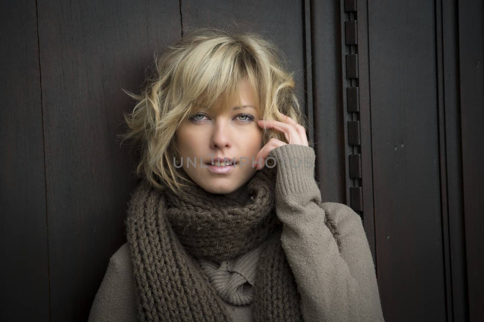 Attractive blonde young woman outside, with winter clothes against wooden door
