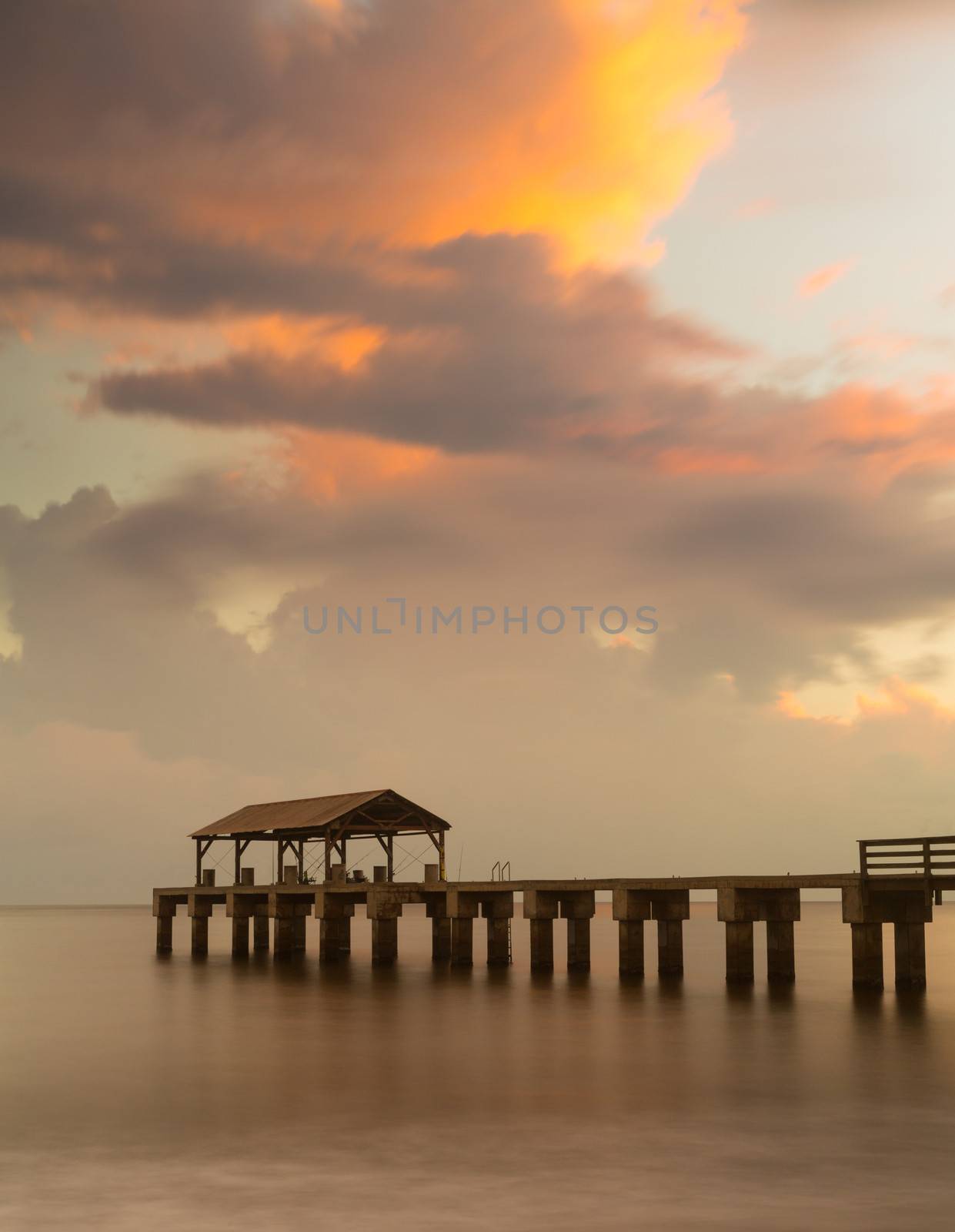 Long exposure image of Waimea pier at sunset blurs the ocean and bathes the structure in the warm glow of the setting sun. Taken on island of Kauai in Hawaiian islands