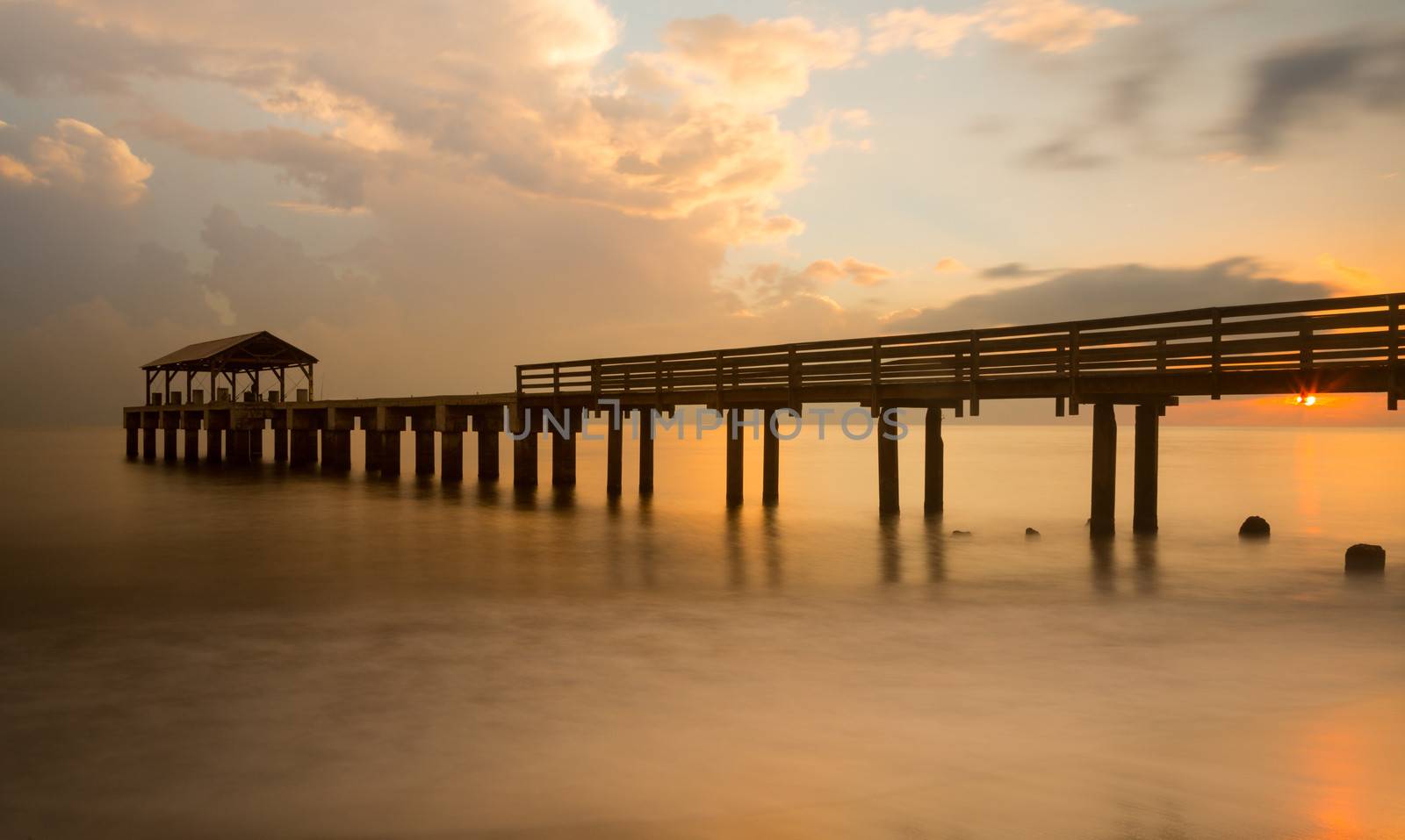 Long exposure image of Waimea pier at sunset blurs the ocean and bathes the structure in the warm glow of the setting sun. Taken on island of Kauai in Hawaiian islands