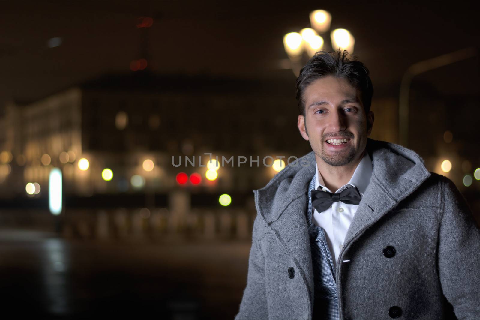 Attractive young man at night in Piazza Vittorio Veneto in Turin, Italy, wearing wool coat and bowtie