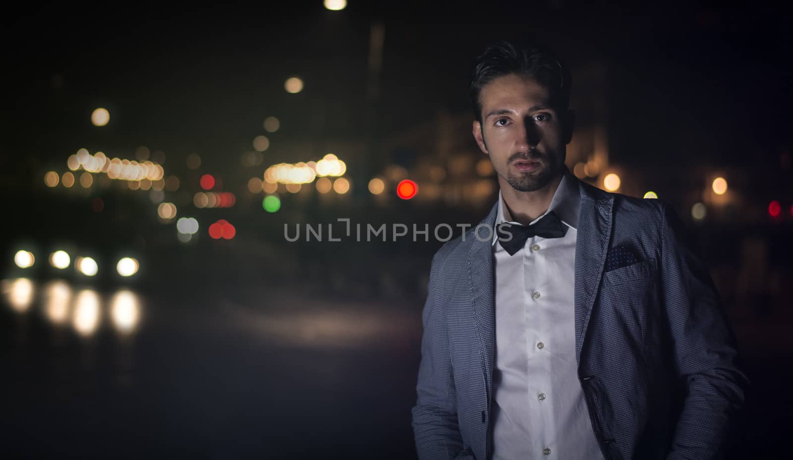 Attractive young man at night with city lights behind him, wearing elegant jacket and bowtie
