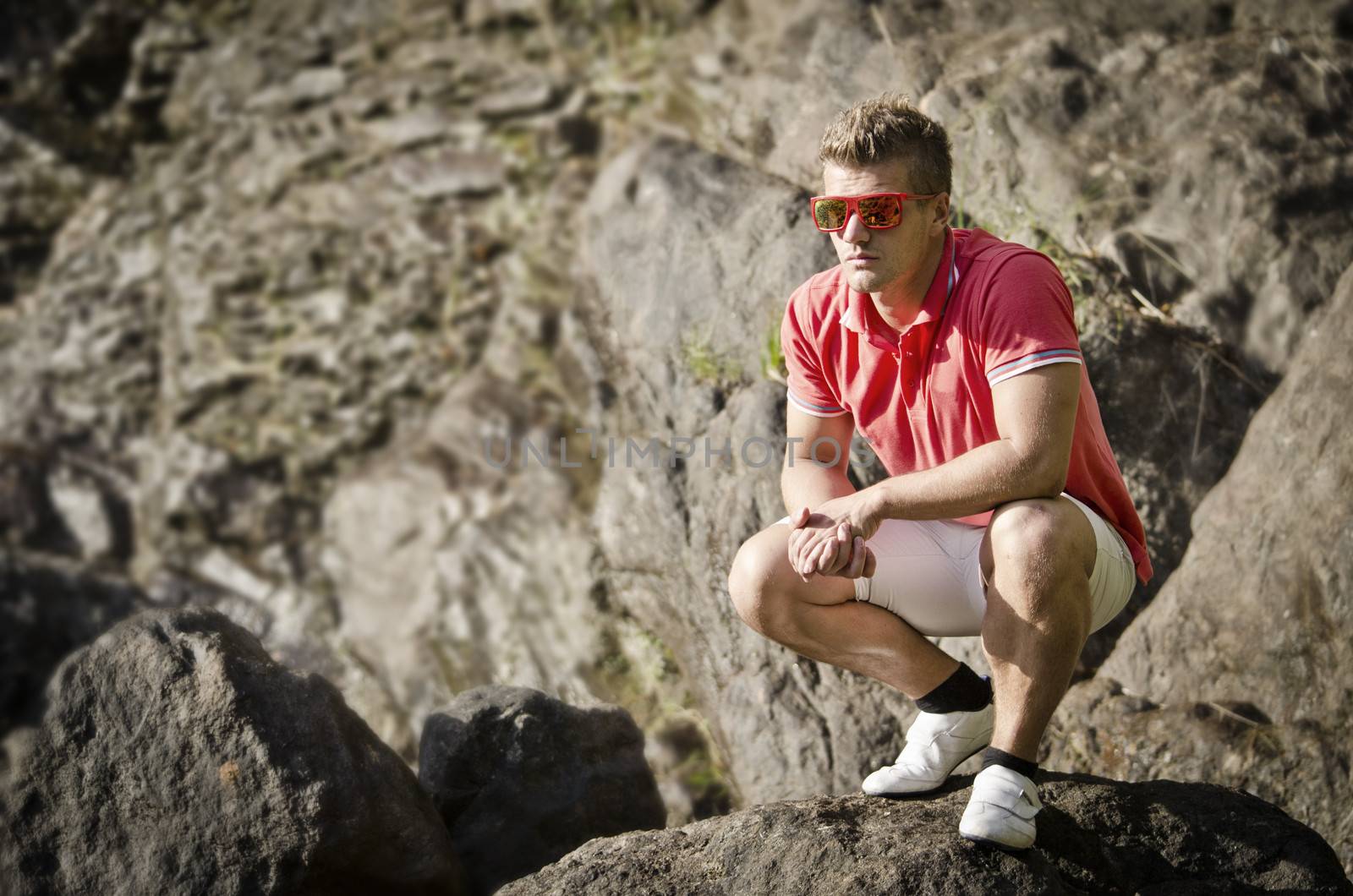 Handsome young man sitting on rock with sunglasses, looking to a side