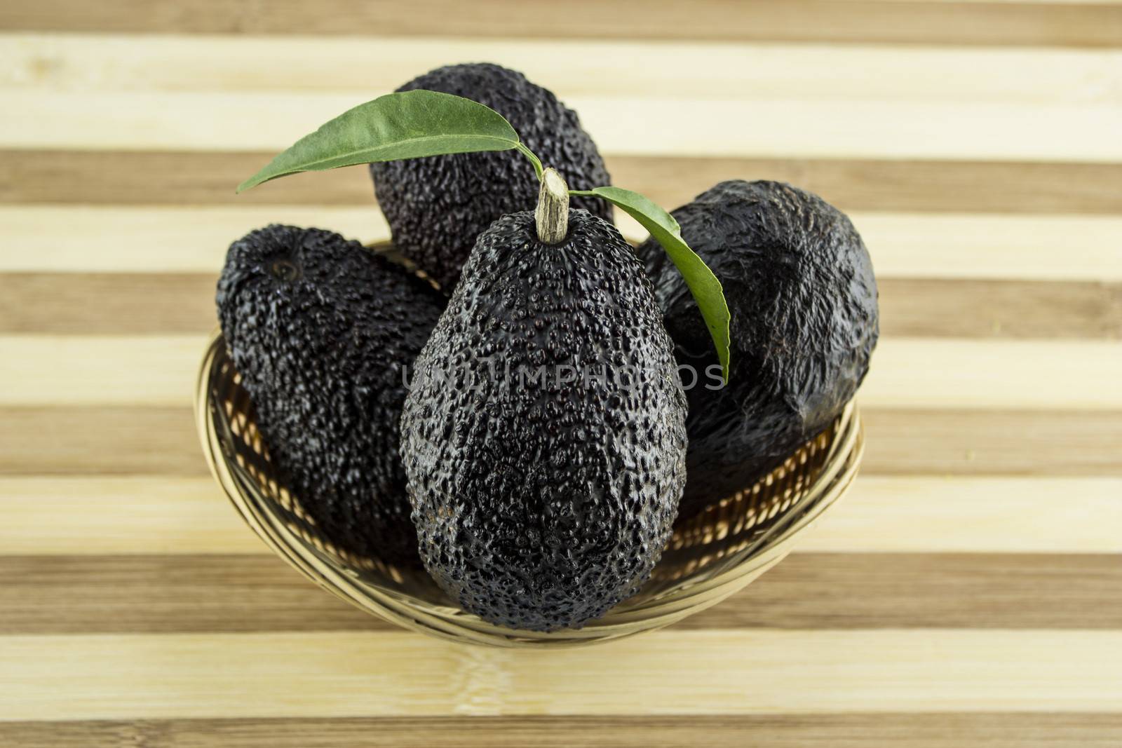 Avocados with leaves on a Dish of straw.