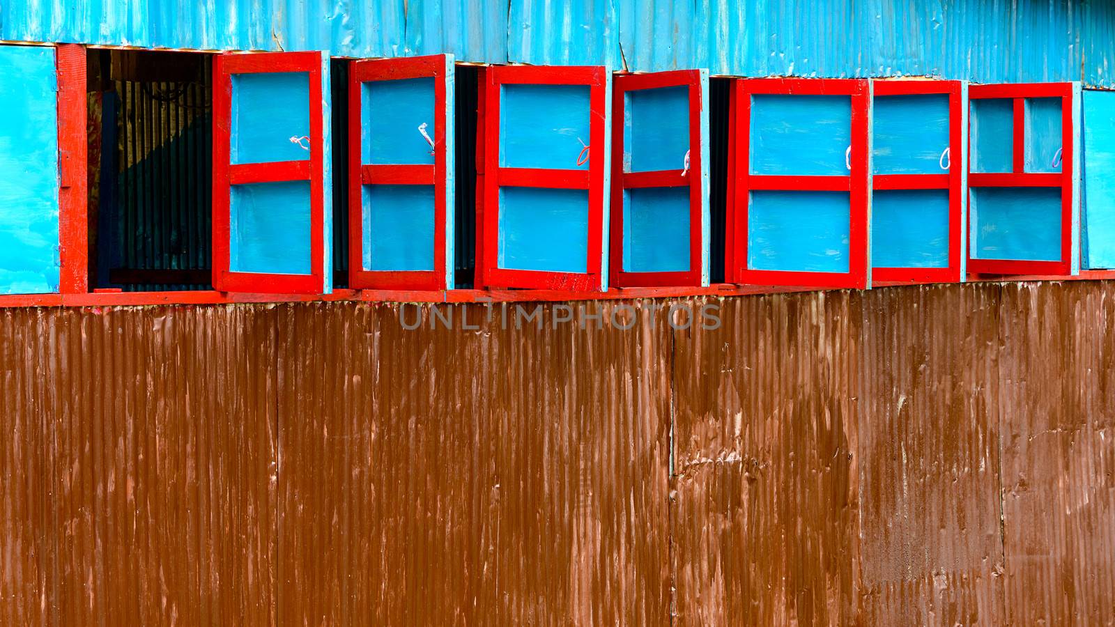 Red and blue wooden windows on corrugated steel wall, Nepal