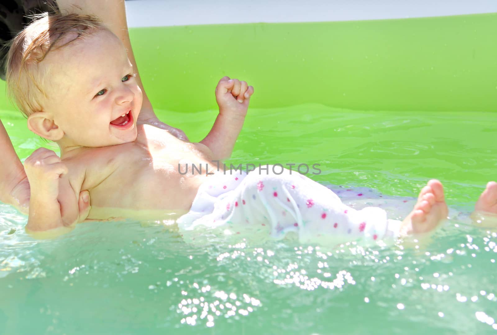 Parent bathing Cheerful Baby Boy in the Pool at Sunny Summer Day