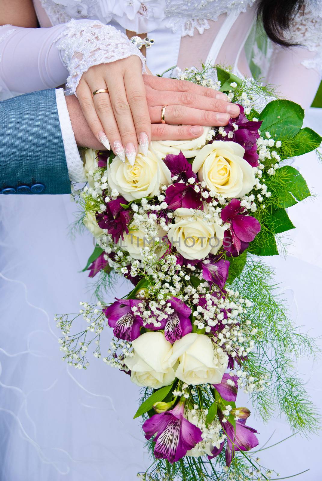 Hands of the groom and the bride with wedding rings on top of the bride's bouquet