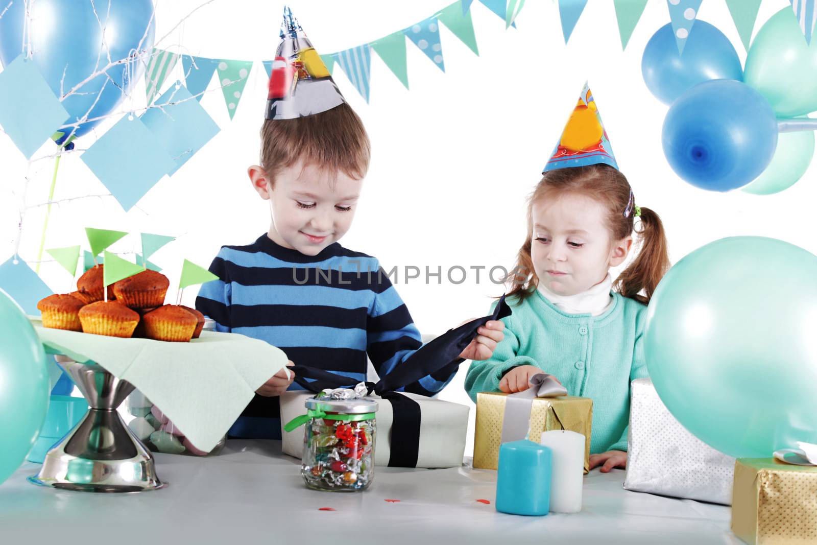 Two children at blue party table openning present over white