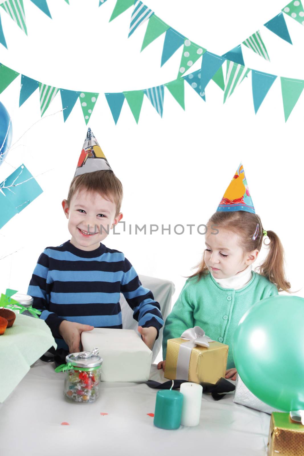 Two children at blue party table openning present over white