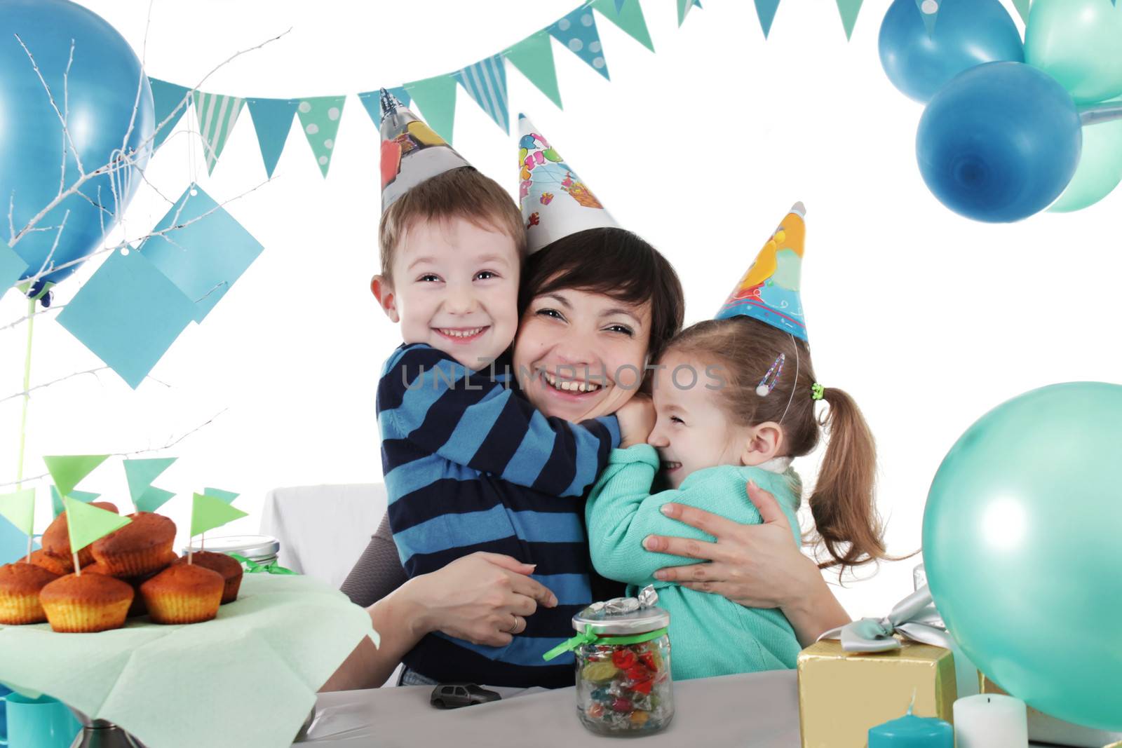 Two children hugging their mother at party table isolated on white